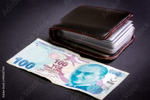 A hundred Turkish lira in selective focus. Credit card wallet and a 100 Turkish lira banknote next to it on an isolated black background. Money, finance, poverty, investment concept.