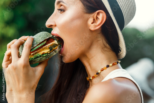 Vegan girl, healthy appearance, holds in her hands and eats a natural, meat-free burger, colored bun, tofu, soy meat, chickpeas. Tropical island Thailand, Bali