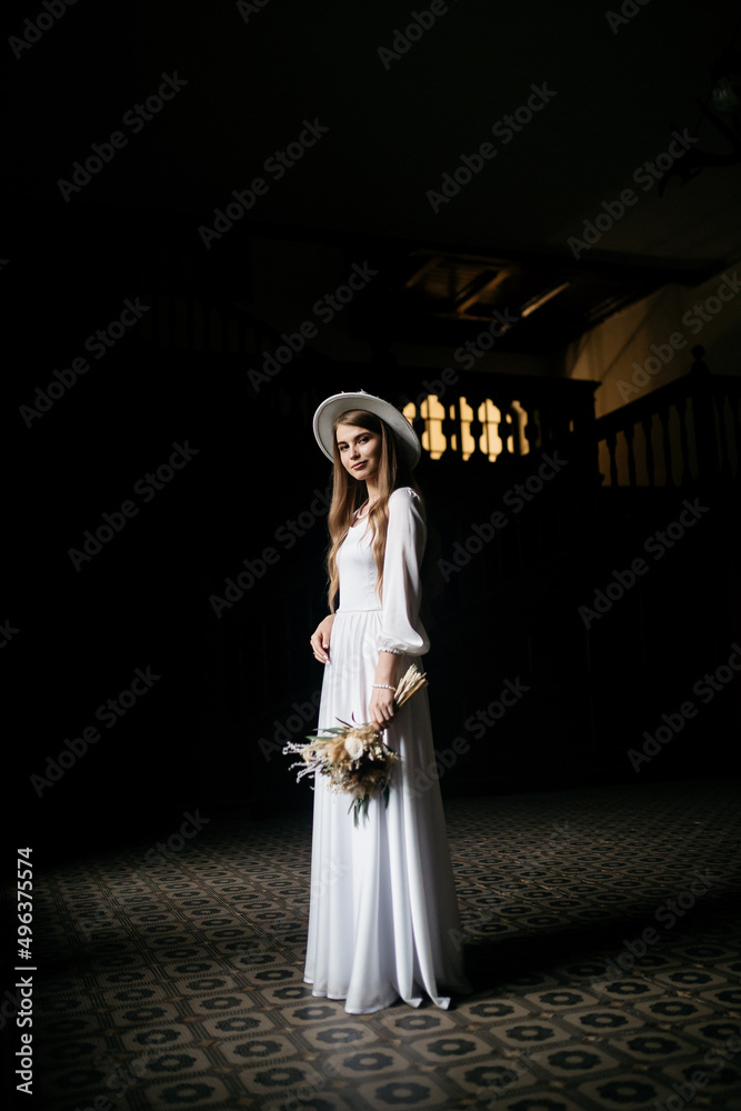 The bride in a hat and a bouquet. Portrait of a bride in a white dress. Portrait of the bride. Young girl in a white wedding dress and hat with a bouquet of flowers.