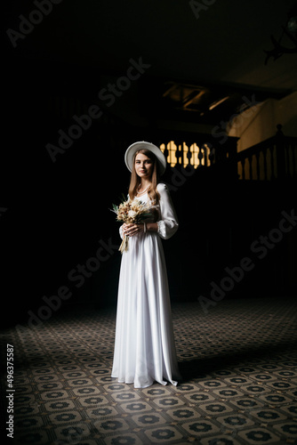 The bride in a hat and a bouquet. Portrait of a bride in a white dress. Portrait of the bride. Young girl in a white wedding dress and hat with a bouquet of flowers.