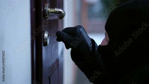 Close-up burglar unlocking entrance door outdoors breaking in house. Side view Caucasian man in mask opening private property robbing. Illegal intrusion and crime concept photo