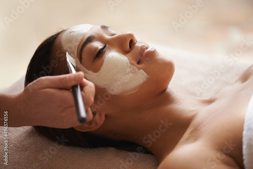 Your skin deserves some pampering. A face mask being applied to a beautiful young woman at a beauty spa. photo