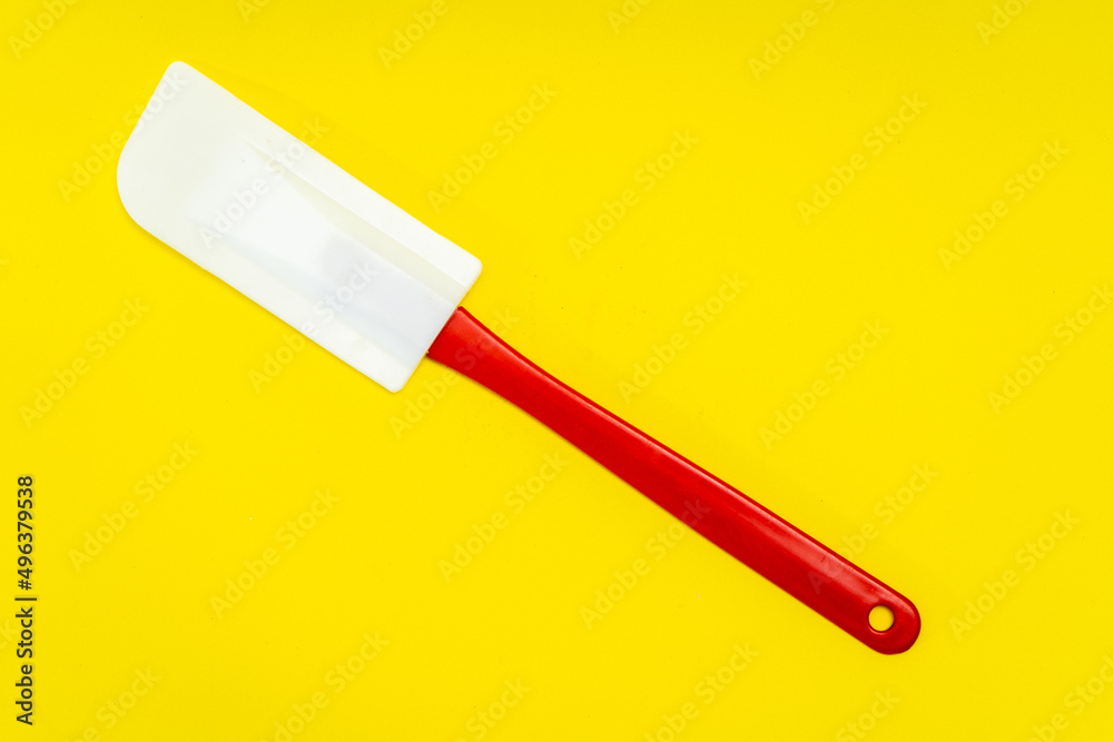 Red and white kitchen spatula made of silicone and plastic insulated on a yellow surface Red and white kitchen spatula made of silicone and plastic insulated on a yellow surface