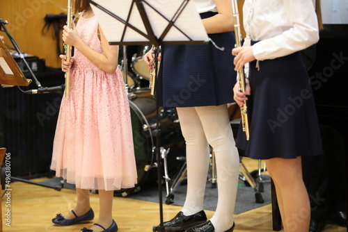 A group of girls young musicians with a musical instrument flute performing at a school concert standing on stage in a festive dress
