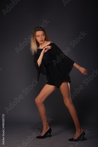 Full-length picture of an attractive sexy young female model posing isolated on a dark background with black dress