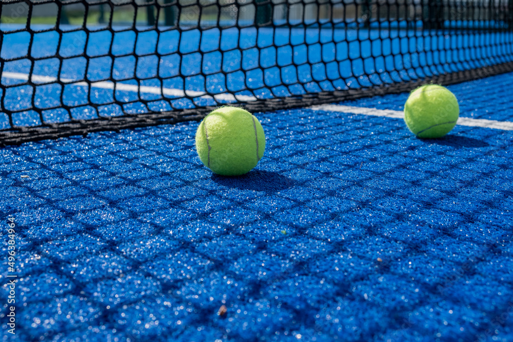 balls in the sun shade of the net on a blue paddle tennis court