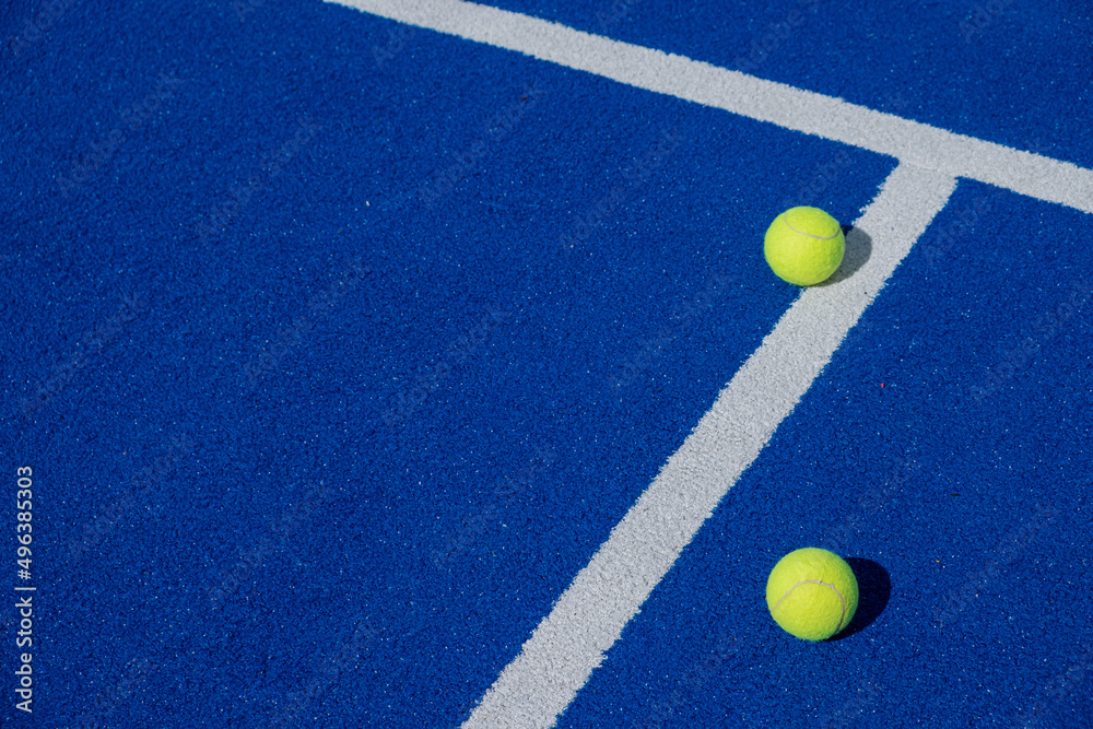 two balls next to the center line on a blue paddle tennis court