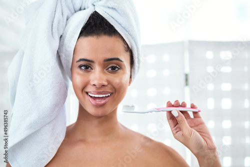 Dont forget to brush. Shot of a beautiful young woman brushing her teeth at home.