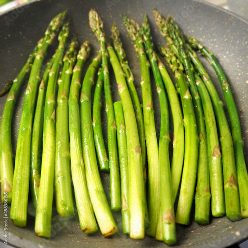 a lot of green asparagus is fried in oil in a gray frying pan.  vegetarianism.  healthy food.  side view