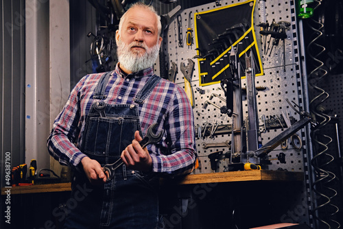 Aged repairman dressed in plaid shirt and overalls in workshop