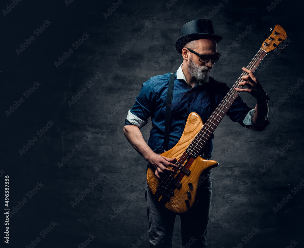 Obraz premium Cool elderly hipster guitarist playing guitar against dark background