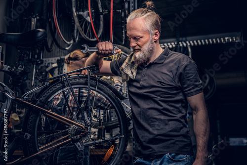 Aged professional repairman posing around bicycle wheel in workshop