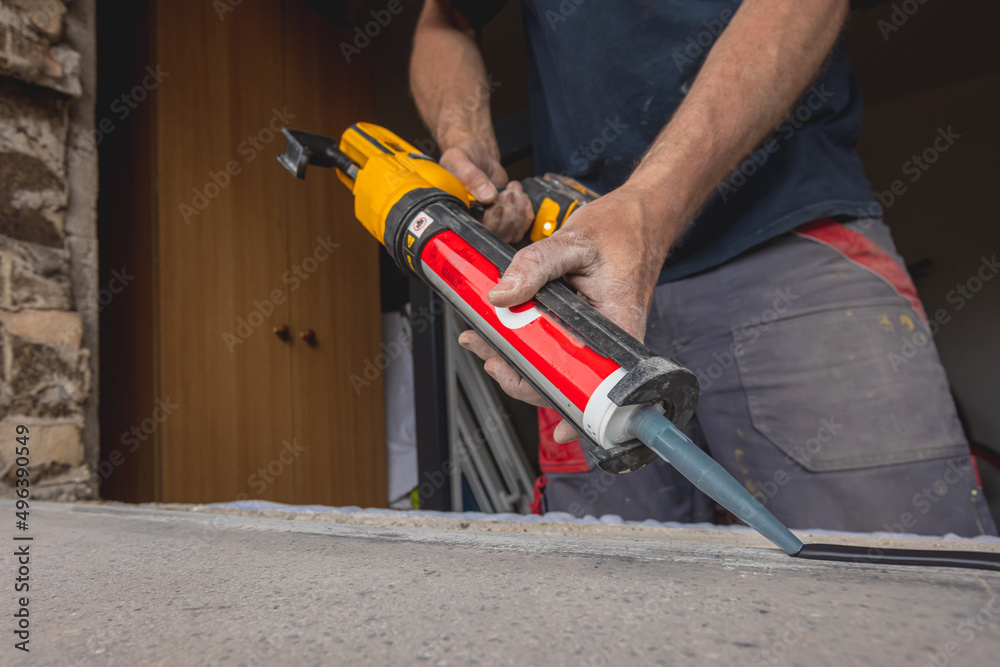 Modern window instalation in an old house. Worker applying sealant or silicone seal onto window shelf or ledge to make a good seal with the new window.