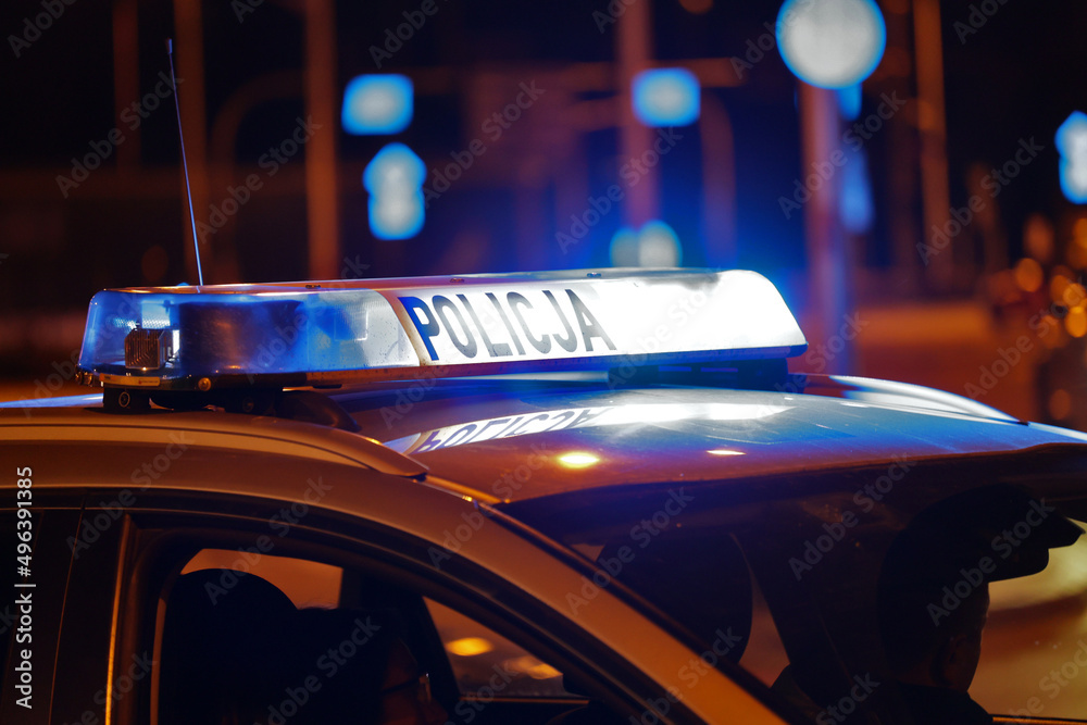 Radiowóz policji na sygnale wieczorem w mieście alarmowo do wypadku na światłach. - obrazy, fototapety, plakaty 
