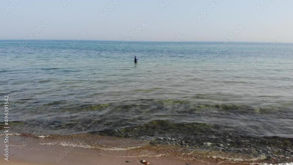 Luftaufnahme von Angler mit Angel in Wathose im Wasser bei Sonne watend per Drohne als Fahrt gefilmt Luftaufnahme von Angler mit Angel in Wathose im Wasser bei Sonne watend per Drohne als Fahrt gefilmt