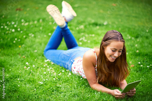 Stumbling upon some great websites. Shot of a young woman using her digital tablet while lying on the grass at the park.