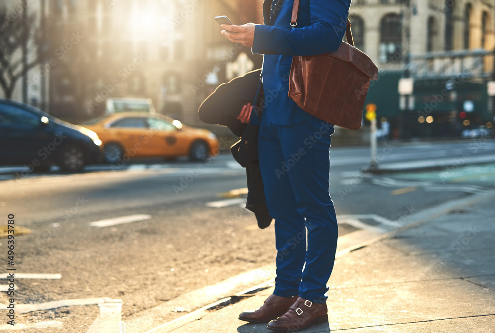 Obraz premium On the busy streets of the city. Low angle shot of a unrecognizable man texting on his phone while waiting for a taxi to take him to work in the morning.