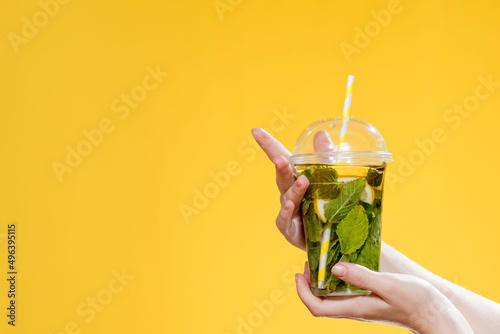 Young woman hand holding a glass of cocktail with mint. Studio photo with yellow background.
