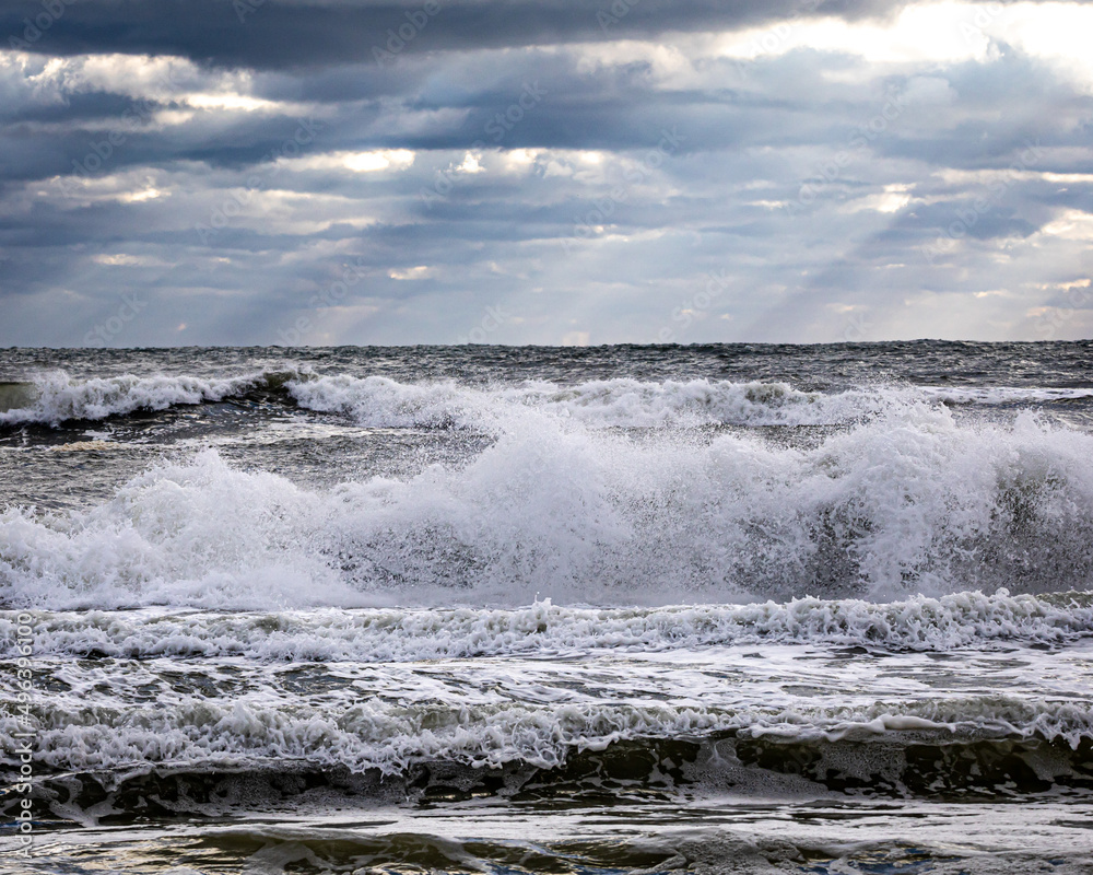 Waves breaking on beach with light rays breaking through storm clouds Waves breaking on beach with light rays breaking through storm clouds