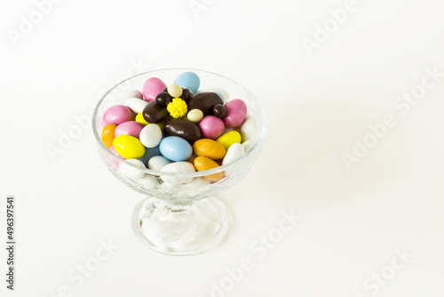 Colorful almond candies are designed in a stylish glass bowl with ball chocolates.White surface with copy space