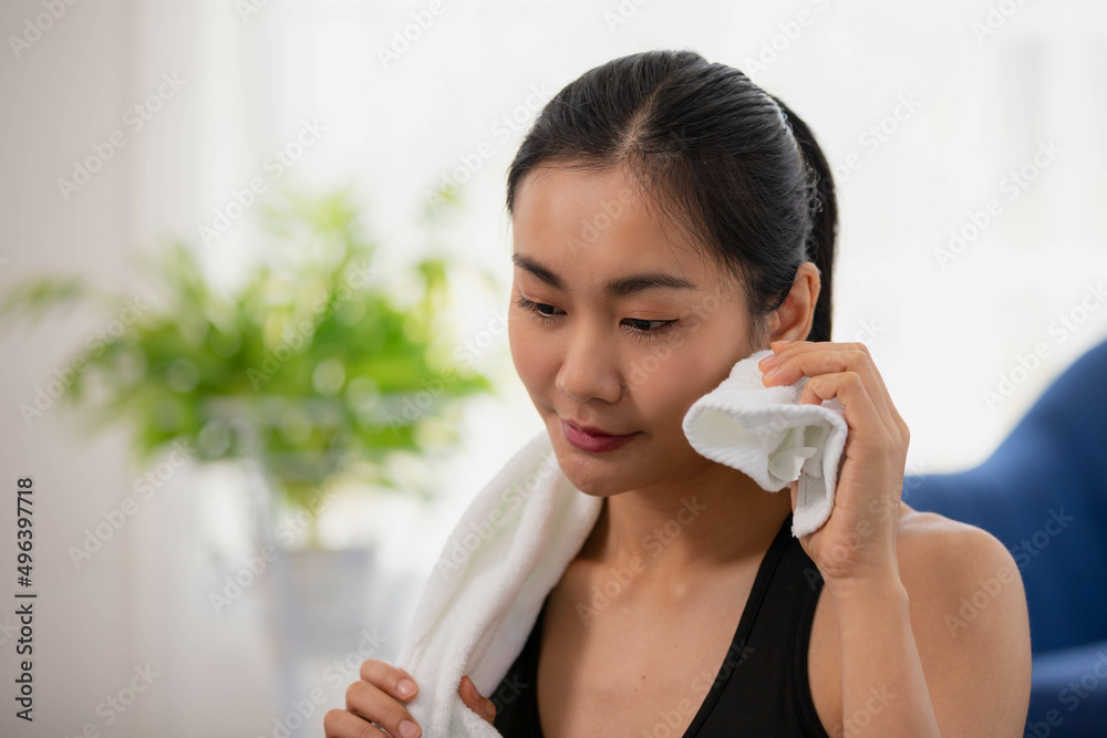 Asian woman in sportswear wiping forehead with towel and while resting after workout in home. Asian woman in sportswear wiping forehead with towel and while resting after workout in home.