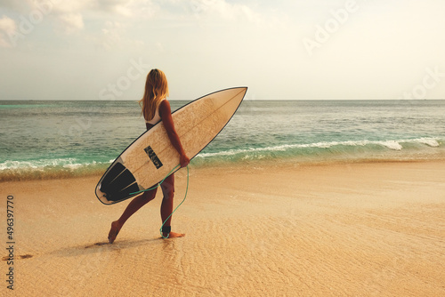 Fotografia blonde surfing girl walking along a sandy beach with a dock for surfing on the b