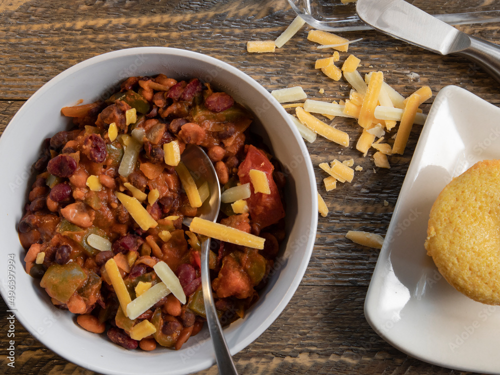 Fototapeta premium Bowl of vegetarian chilli with cornbread top view on a natural wood table