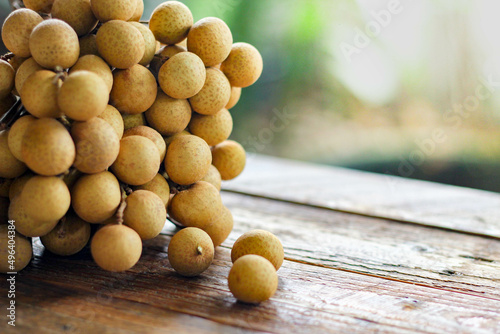 bunch of longan is placed on a wooden table with green leaves behind.