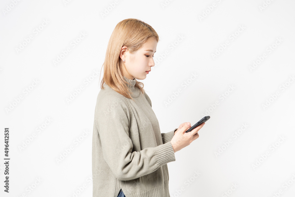 白い背景の前に立ってスマホを使う若い女性 白い背景の前に立ってスマホを使う若い女性