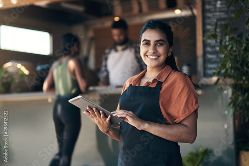 Lets get you seated. Shot of an attractive young woman standing outside her restaurant and using a digital tablet.