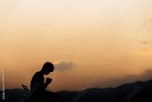 Silhouette of a man holding hands and prayer on mountain at sunset. concept of religion.
