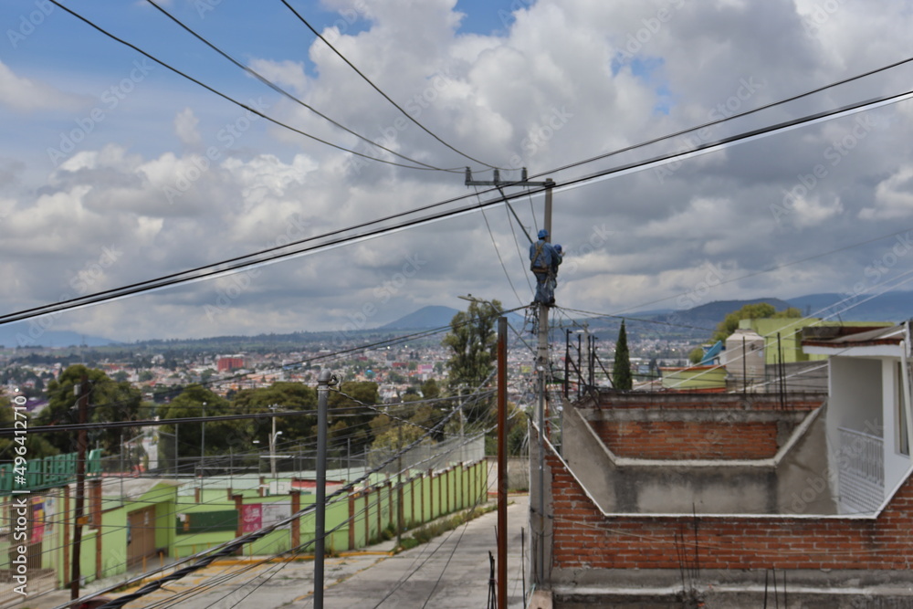 Electricistas reparando cables del poste de luz, entre las casas de una ciudad durante el día soleado. Electricistas reparando cables del poste de luz, entre las casas de una ciudad durante el día soleado.