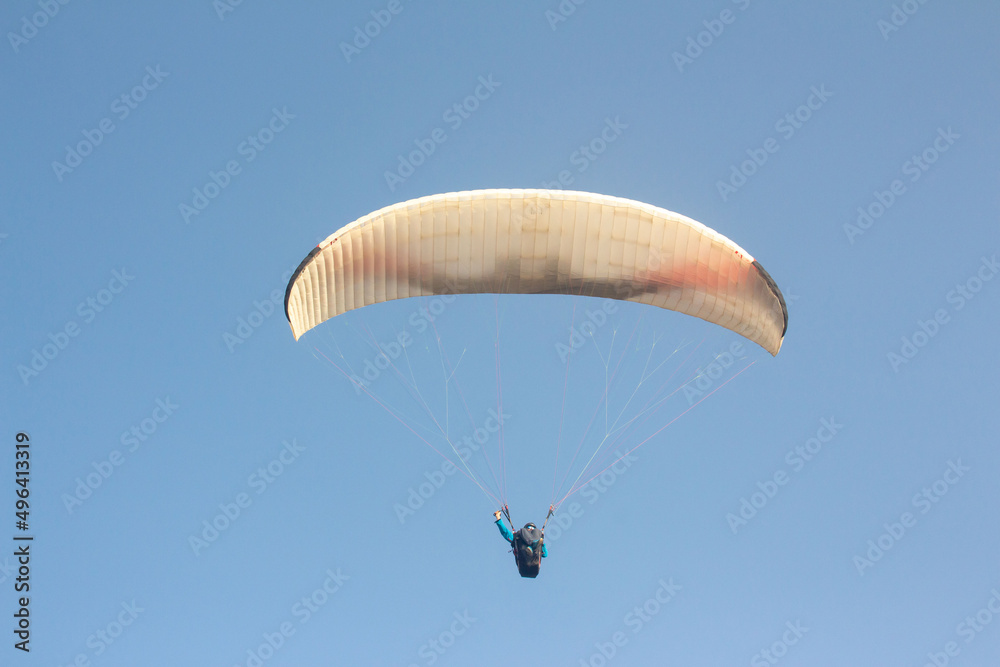 Paraglider flying along in the sky , paraglide flying gliding on a clear blue sky, white paragliding Paraglider flying along in the sky , paraglide flying gliding on a clear blue sky, white paragliding
