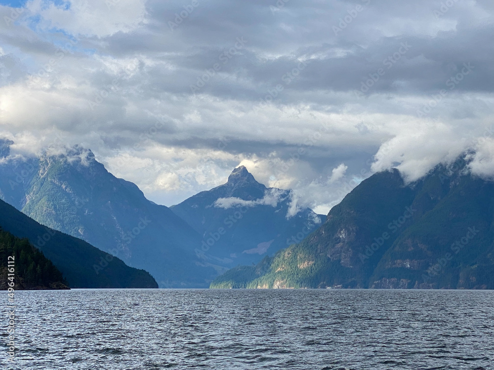 Jervis Inlet north in British Columbia, surrounded by high, rugged peaks of the Coast Mountains and beautiful water clouds in the sky. Inlet approach to Malibu Rapids