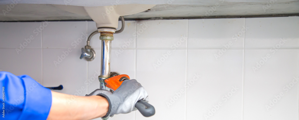 Technician plumber using a wrench to repair a water pipe under the sink. Concept of maintenance, fix water plumbing leaks, replace the kitchen sink drain, cleaning clogged pipes is dirty or rusty. Technician plumber using a wrench to repair a water pipe under the sink. Concept of maintenance, fix water plumbing leaks, replace the kitchen sink drain, cleaning clogged pipes is dirty or rusty.