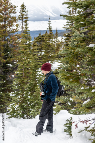 Man, photogrpaher hiking in the boreal forest of Canada with snow covered landscape and spruce trees surrounding. 