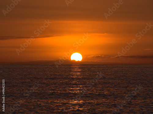 Fototapeta Naklejka Na Ścianę i Meble -  Sunset above the Atlantic Ocean with bright sun disappearing between low clouds on the horizon and orange sky viewed from the coast of Gran Canaria.