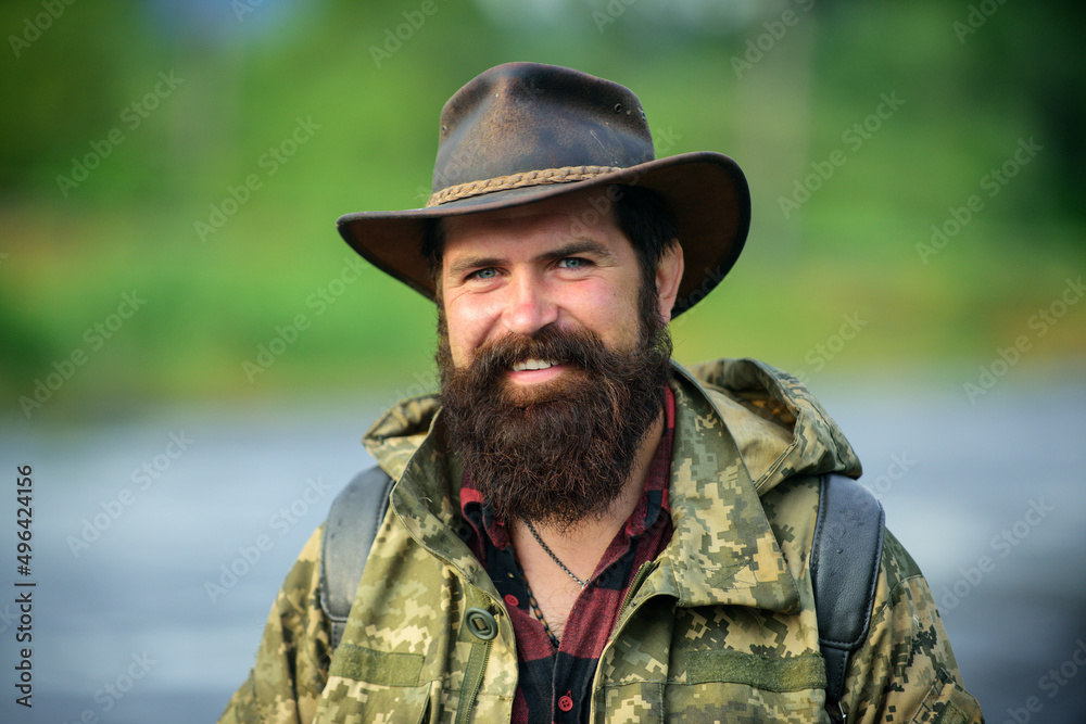 Portrait of happy man traveler with backpack hiking outdoor. Travel lifestyle countryside and adventure concept. Portrait smiling traveller bearded man in cowboy hat.