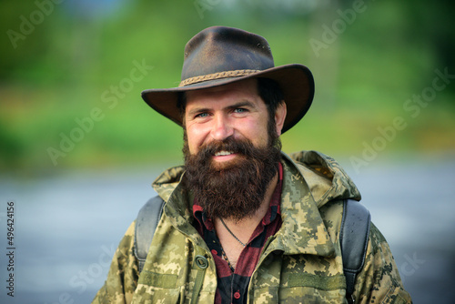 Portrait of happy man traveler with backpack hiking outdoor. Travel lifestyle countryside and adventure concept. Portrait smiling traveller bearded man in cowboy hat.