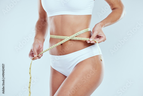 Measure up. Cropped shot of an unrecognizable young woman measuring her waist against a grey background.