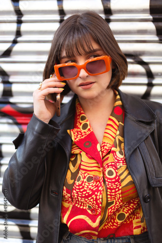 Beautiful young caucasian woman talking on phone outdoors. She wears a cute trendy outfit and sunglasses. Modern urban fashion concept.