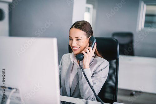 фотографія A friendly secretary answering phone call and using computer at office