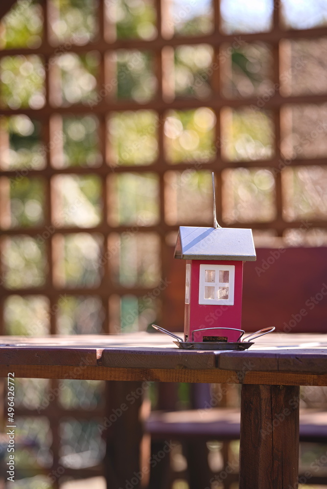 Red feeder for birds in the shape of a house on a background of openwork pergola in the garden Red feeder for birds in the shape of a house on a background of openwork pergola in the garden
