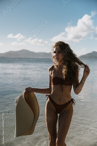 Beautiful young woman in a bikini swimsuit on a tanned body and a straw hat on the Seychelles beach on the island of Mahe or La Digue