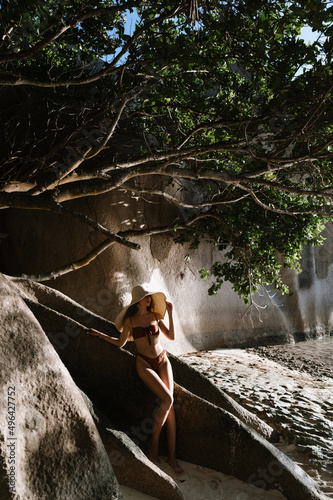 Beautiful young woman in a bikini swimsuit on a tanned body and a straw hat on the Seychelles beach on the island of Mahe or La Digue