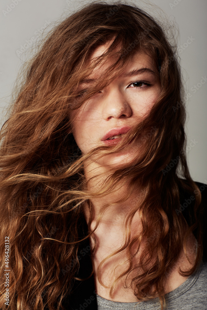 Shes a confident teen. Closeup portrait of an attractive young with her hair in her face against a gray background. Shes a confident teen. Closeup portrait of an attractive young with her hair in her face against a gray background.