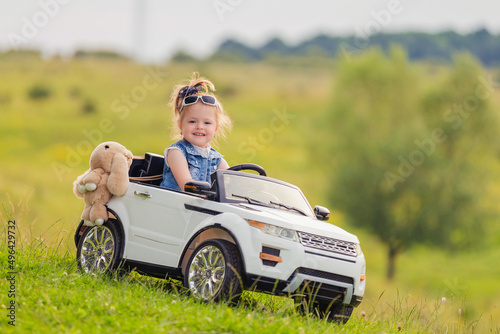 little girl rides on a children's car on a green lawn
