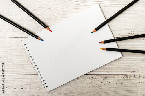 Notebook with white sheets and colored pencils for drawing on white wooden background 