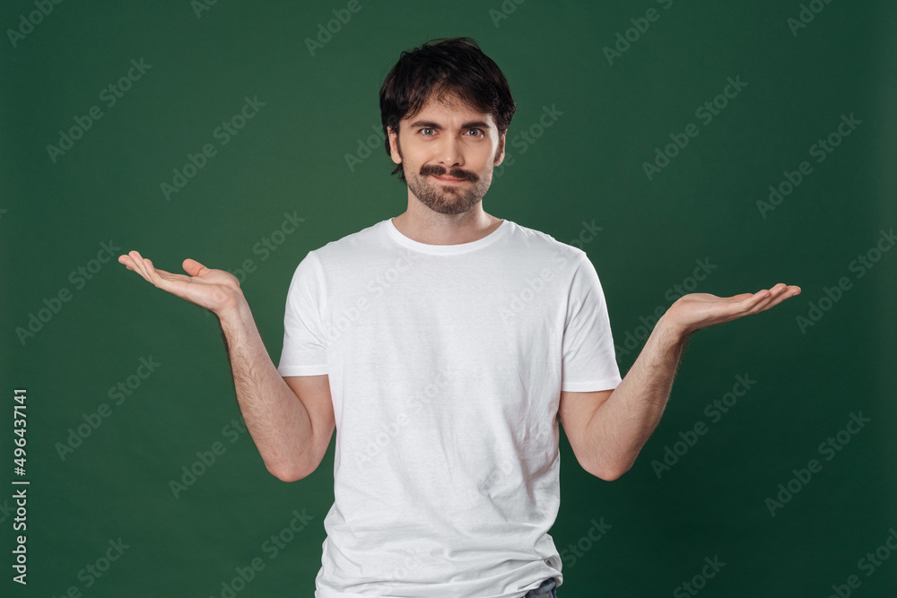 On a dark green background, a young man in a white T-shirt spread his arms to the sides and looks straight into the frame On a dark green background, a young man in a white T-shirt spread his arms to the sides and looks straight into the frame