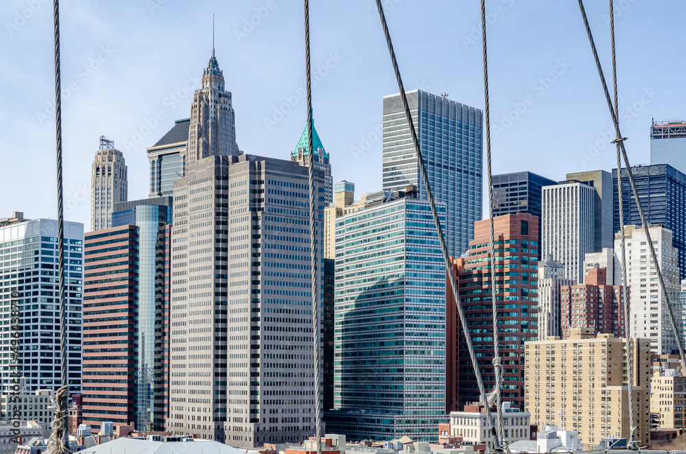 Skyline of Manhattan during daytime with clear sky with wire ropes of Brooklyn Bridge in the forefront, horizontal